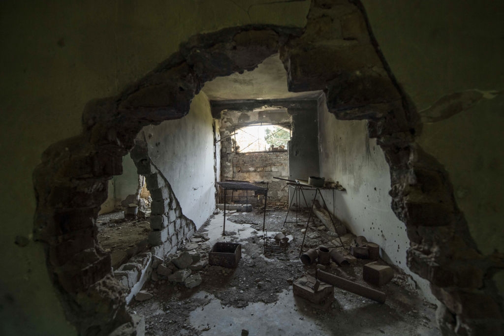 Dilapidated room with a large hole in the wall, scattered debris, and an old window partially covered by rubble