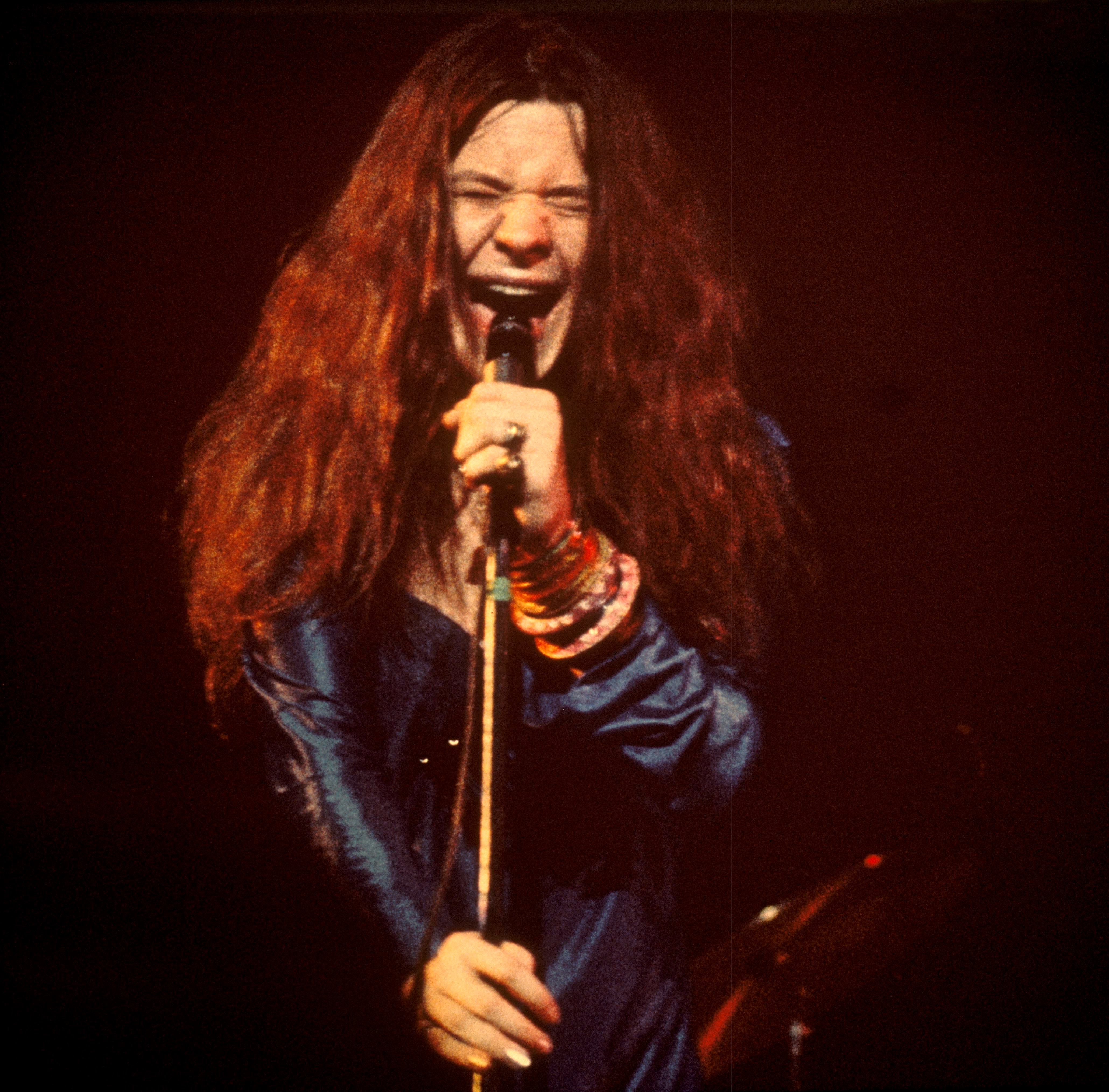 A performer energetically singing on stage, wearing a flowing outfit with multiple bracelets, showcasing lively expression and passion