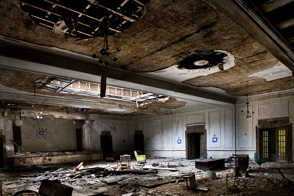 Abandoned, decaying room with collapsed ceiling, debris scattered on the floor, and peeling walls