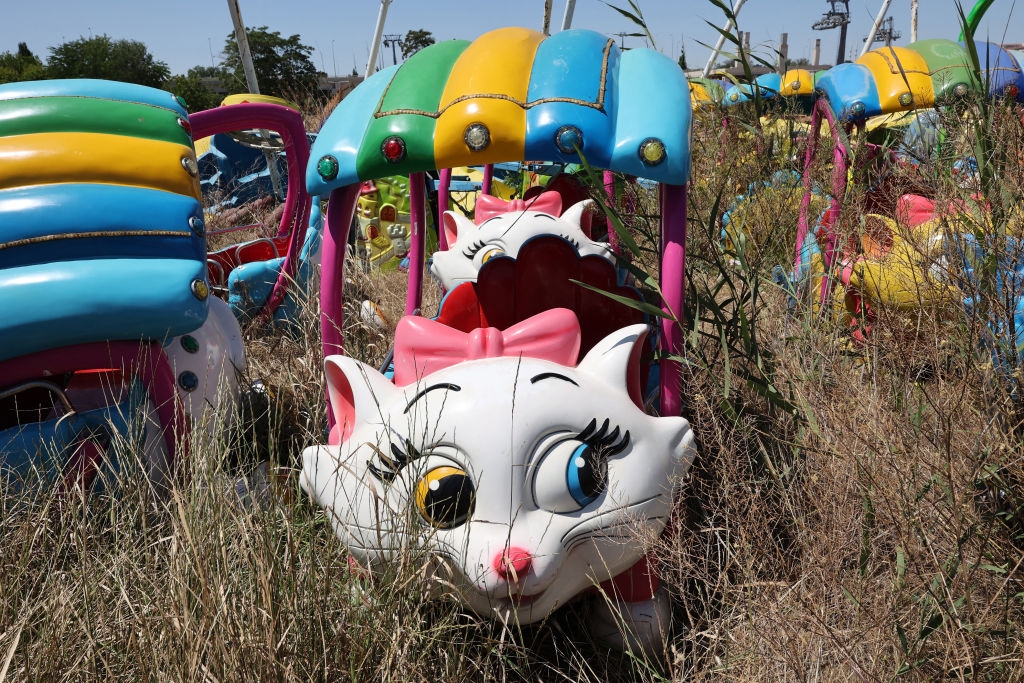 Abandoned amusement park ride shaped like a cat's face with plants growing around it