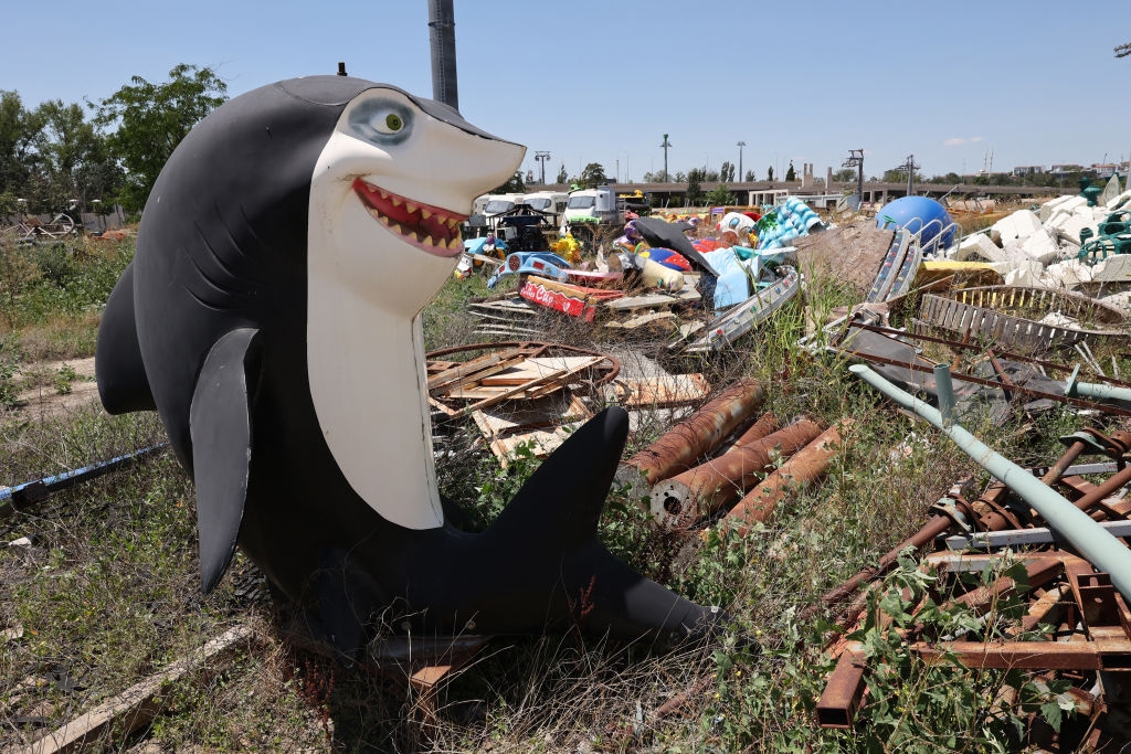 Shark sculpture with big grin in a field of scattered debris and discarded items