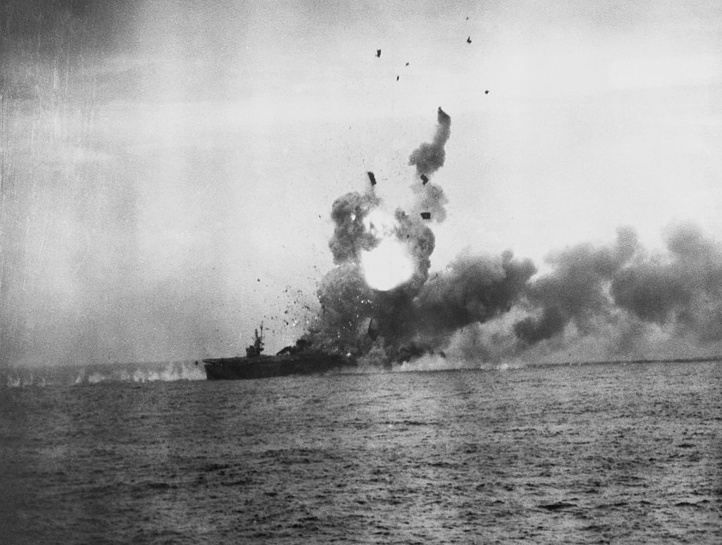 A ship at sea is engulfed in a large explosion, with debris and smoke rising into the sky