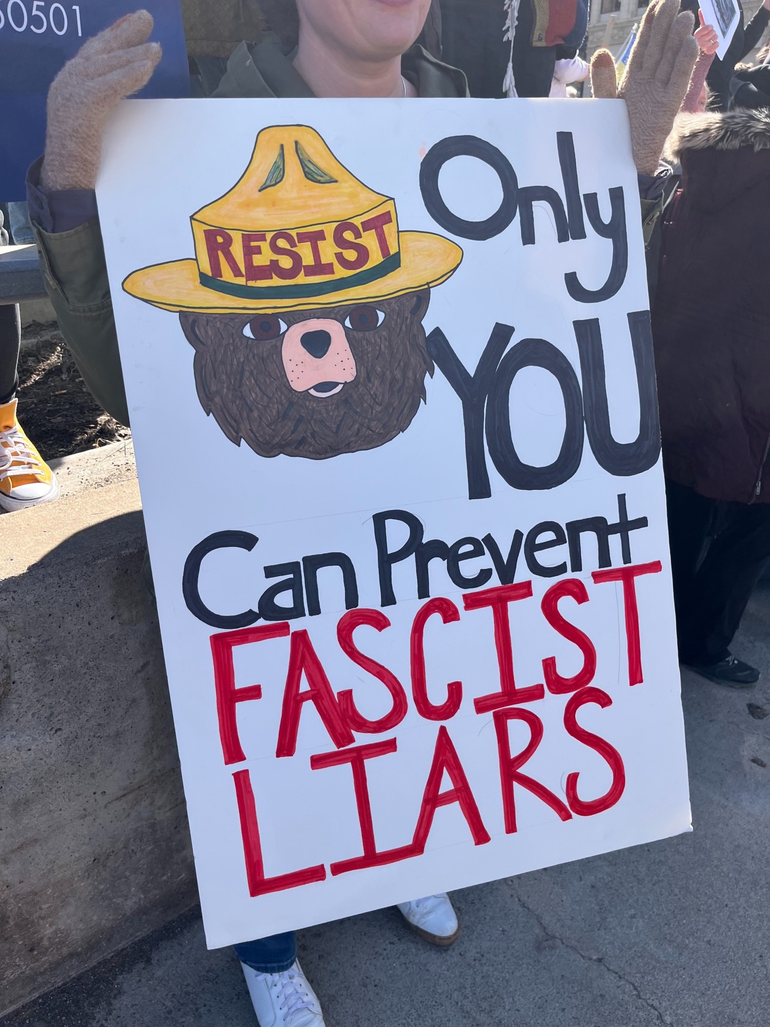 Person holds sign with illustrated bear in a hat, text reads: "Only YOU can prevent fascist liars"