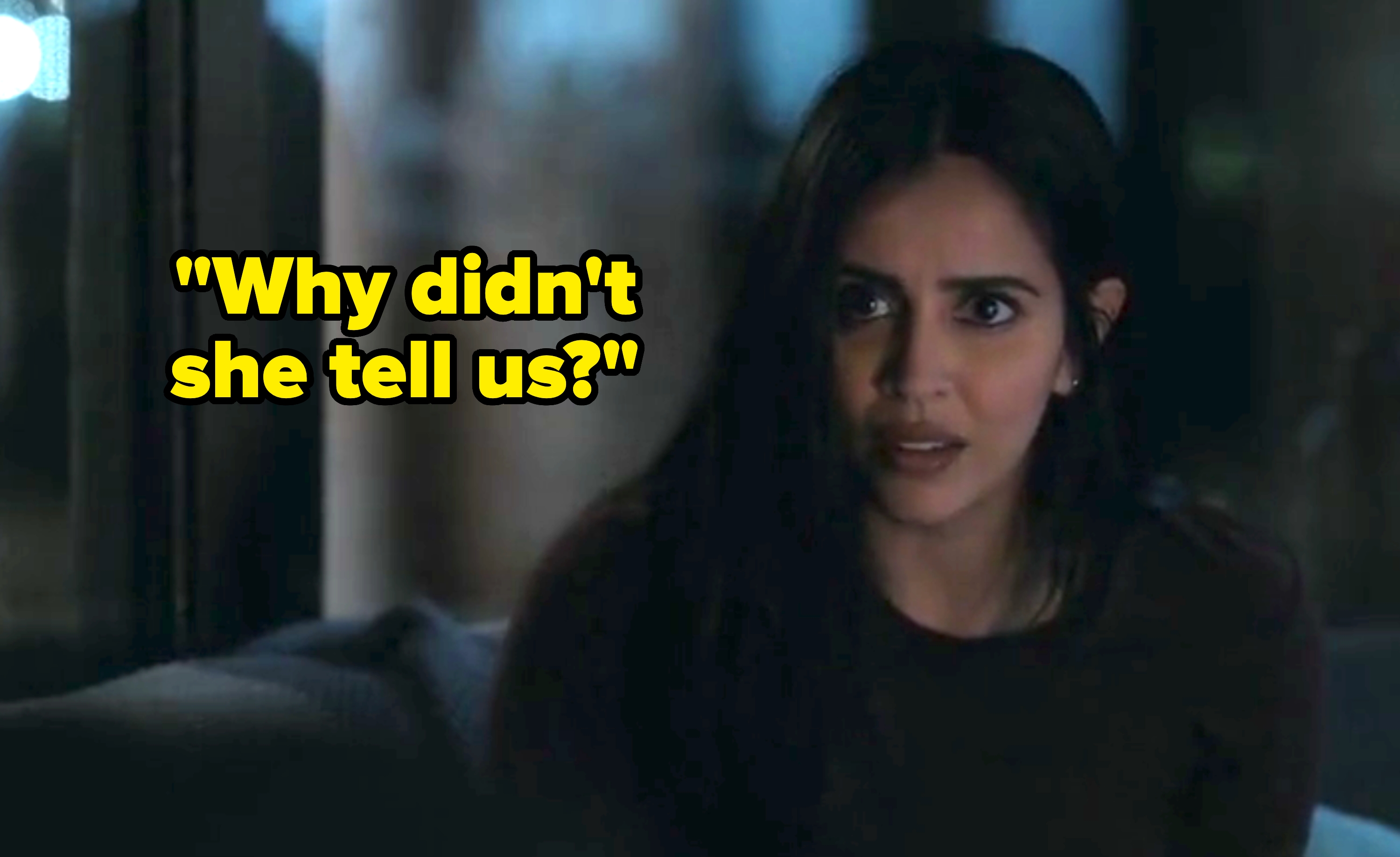 A person with long hair looks concerned while sitting indoors, facing slightly right