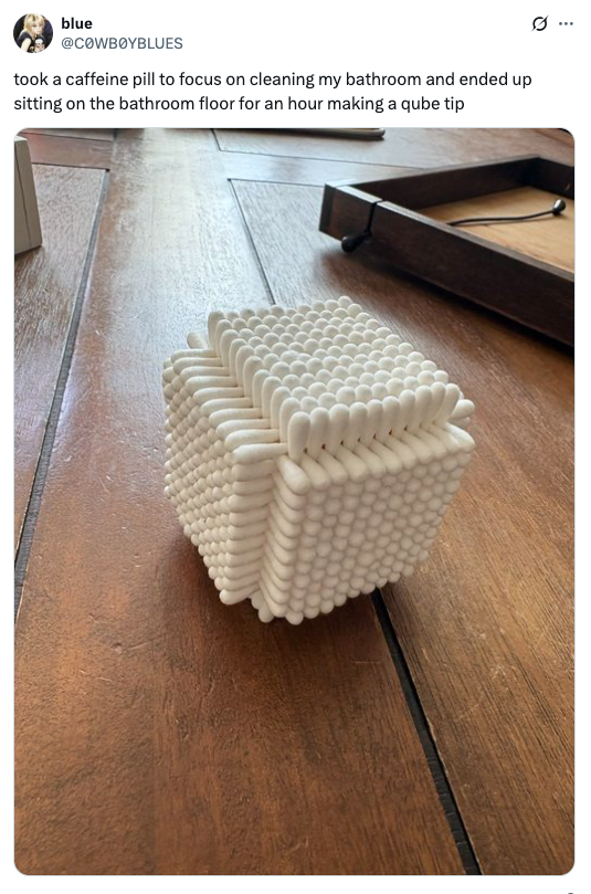 A white cube made of interwoven cotton swabs on a wooden floor; tweet caption jokes about procrastination