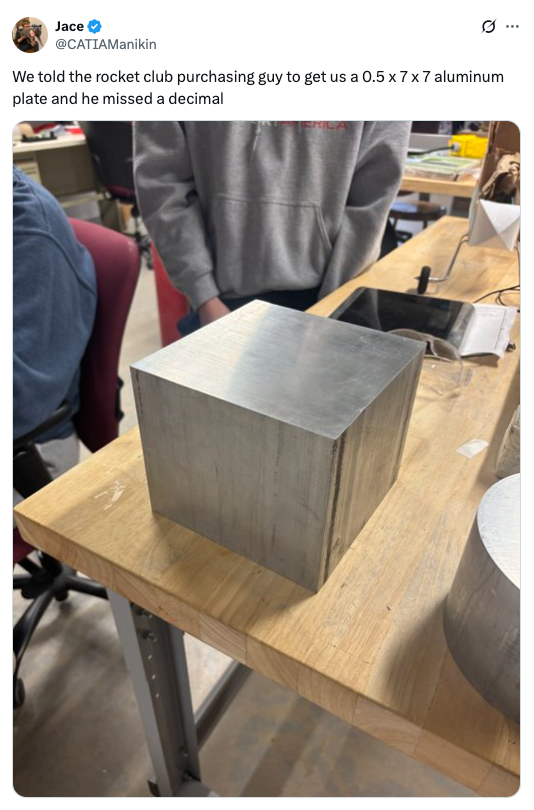 A large aluminum cube is on a table, with someone standing nearby. A tweet above jokes about a decimal mistake in a purchasing order for the cube