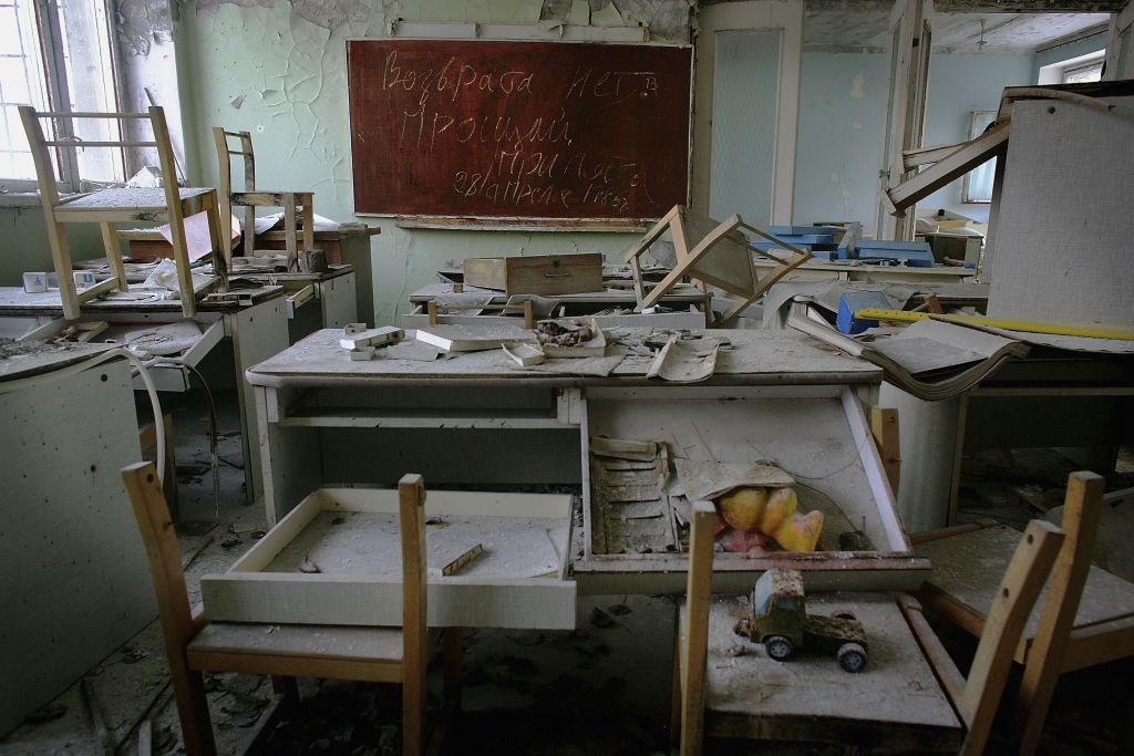 Abandoned classroom with overturned desks and scattered debris, conveying neglect and decay
