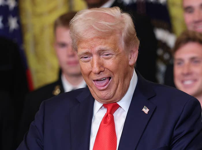 A person in a suit holding a football and a ring, smiling widely, surrounded by others in formal attire