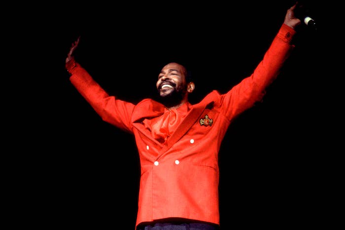 A person joyfully raises their arms while wearing a stylish double-breasted suit with a unique emblem on the jacket