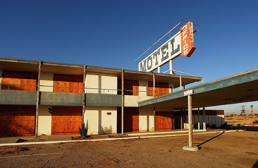 Abandoned motel with boarded windows and faded sign in a desert setting under a clear sky