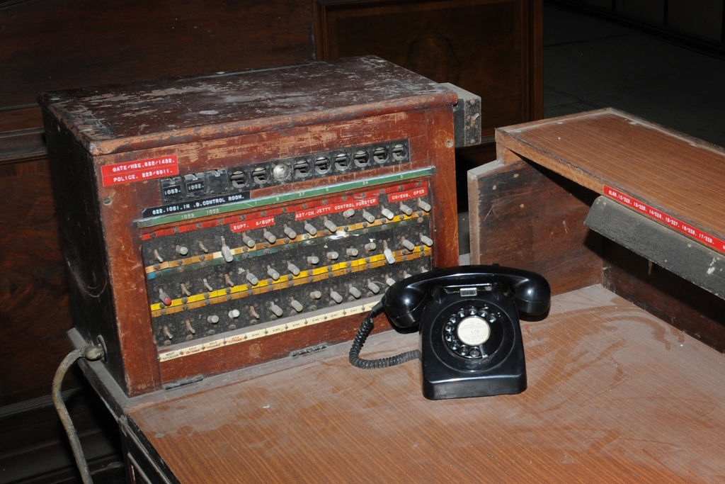 Vintage telephone switchboard with rotary phone on a wooden desk, covered in dust