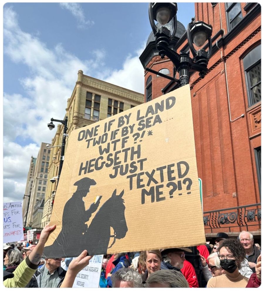 Protest sign referencing historical quote with humorous modern twist in a city street setting