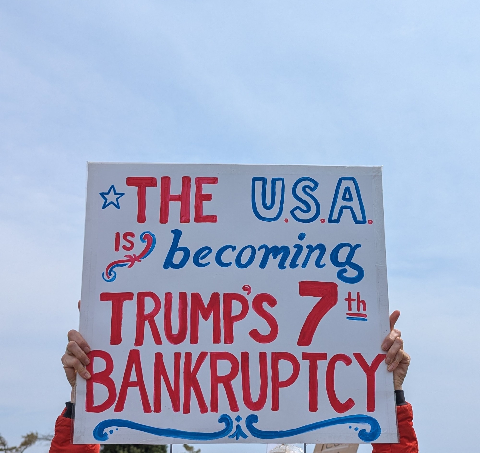 Sign reads: "The USA is becoming Trump's 7th bankruptcy."