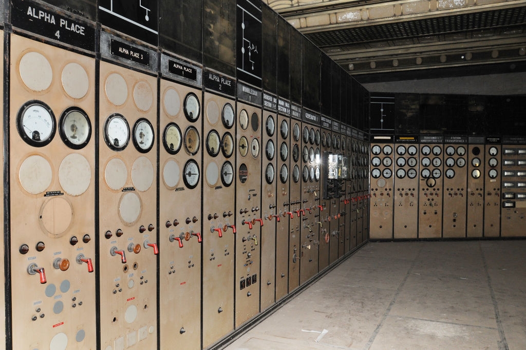 Control room with vintage dials, switches, and meters on panels, likely for industrial or power plant operations