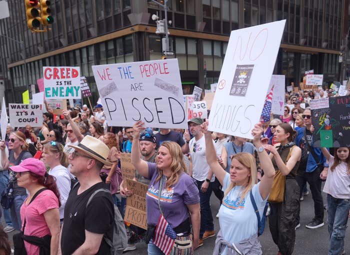 People at a protest hold signs with messages expressing discontent, including &quot;We the people are pissed&quot; and &quot;No kings.&quot;