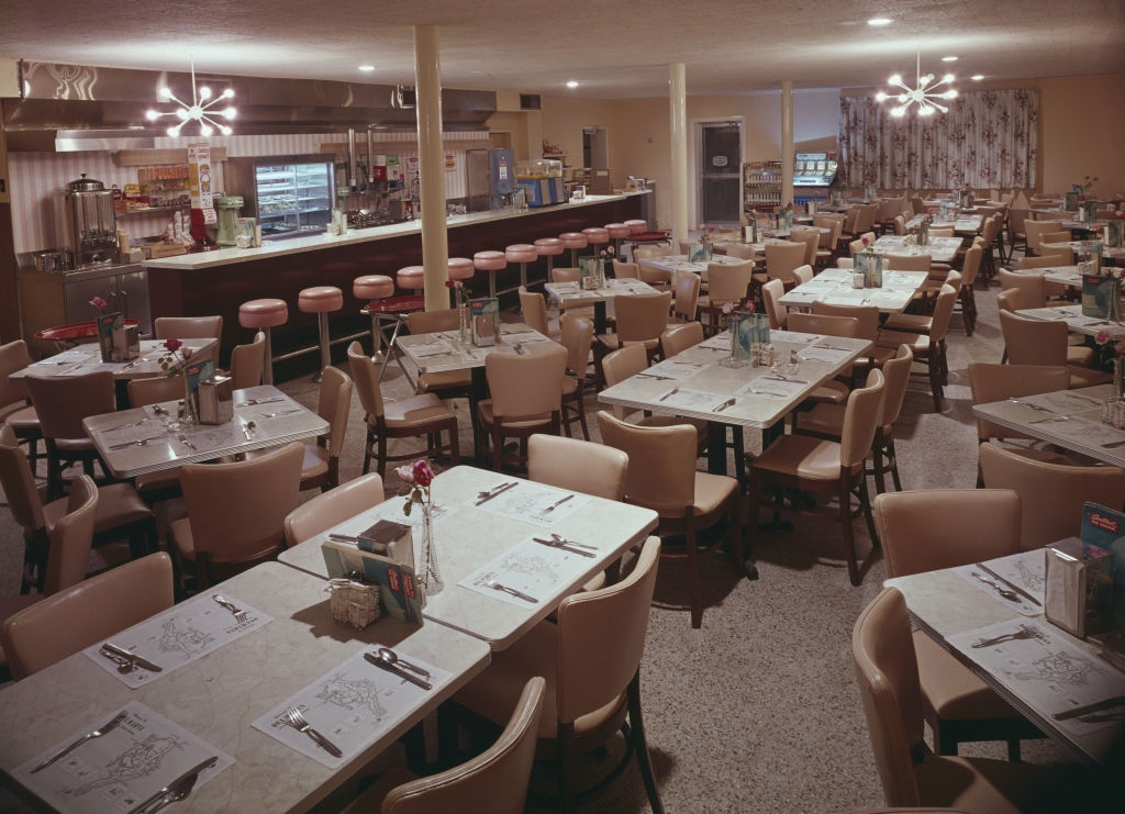 A retro diner with multiple tables, cushioned stools at the counter, and vintage decor, evoking a classic mid-20th century American restaurant style