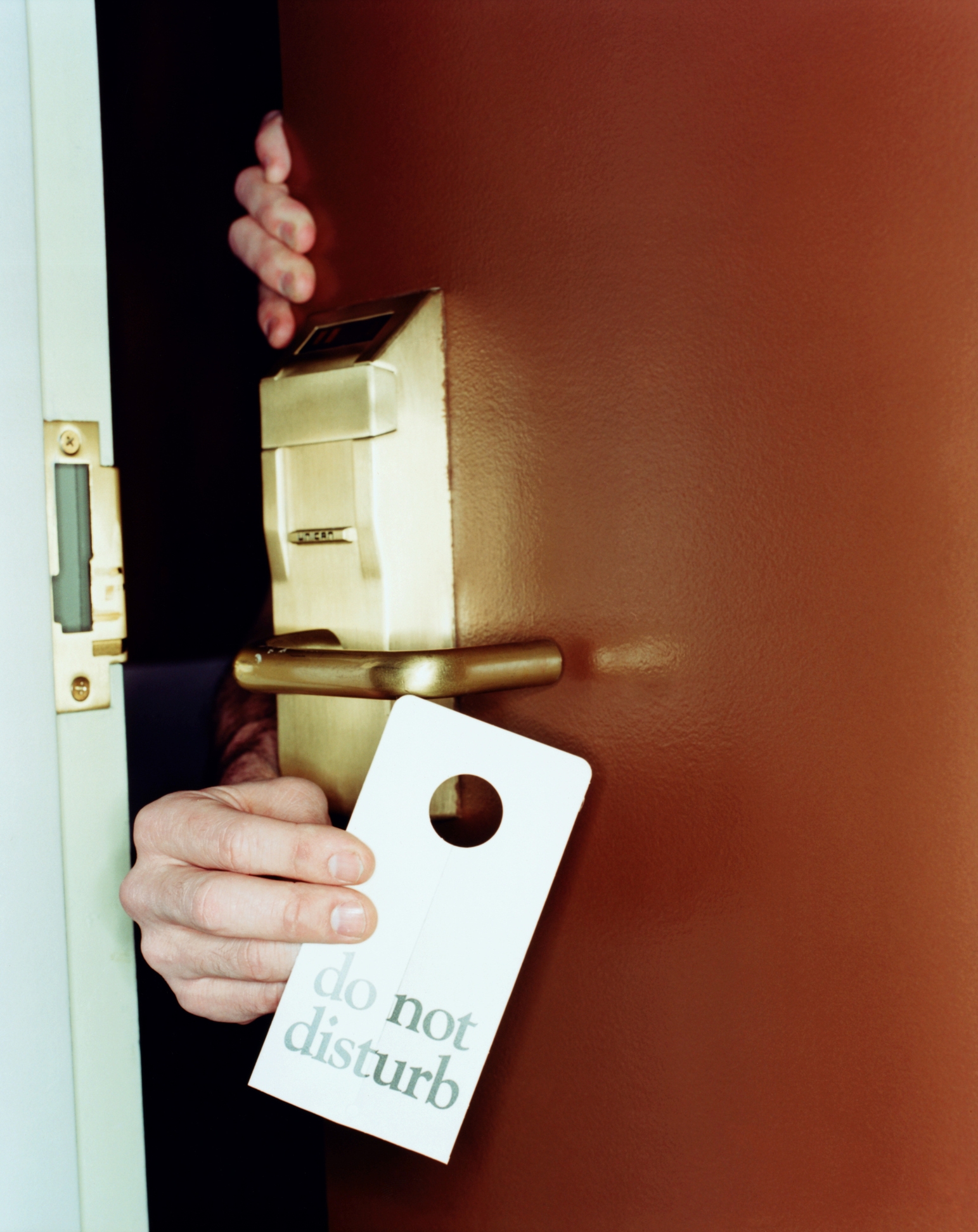 Hand holding a "Do Not Disturb" sign on a hotel door handle, partially opened door, hinting at privacy or intimacy theme