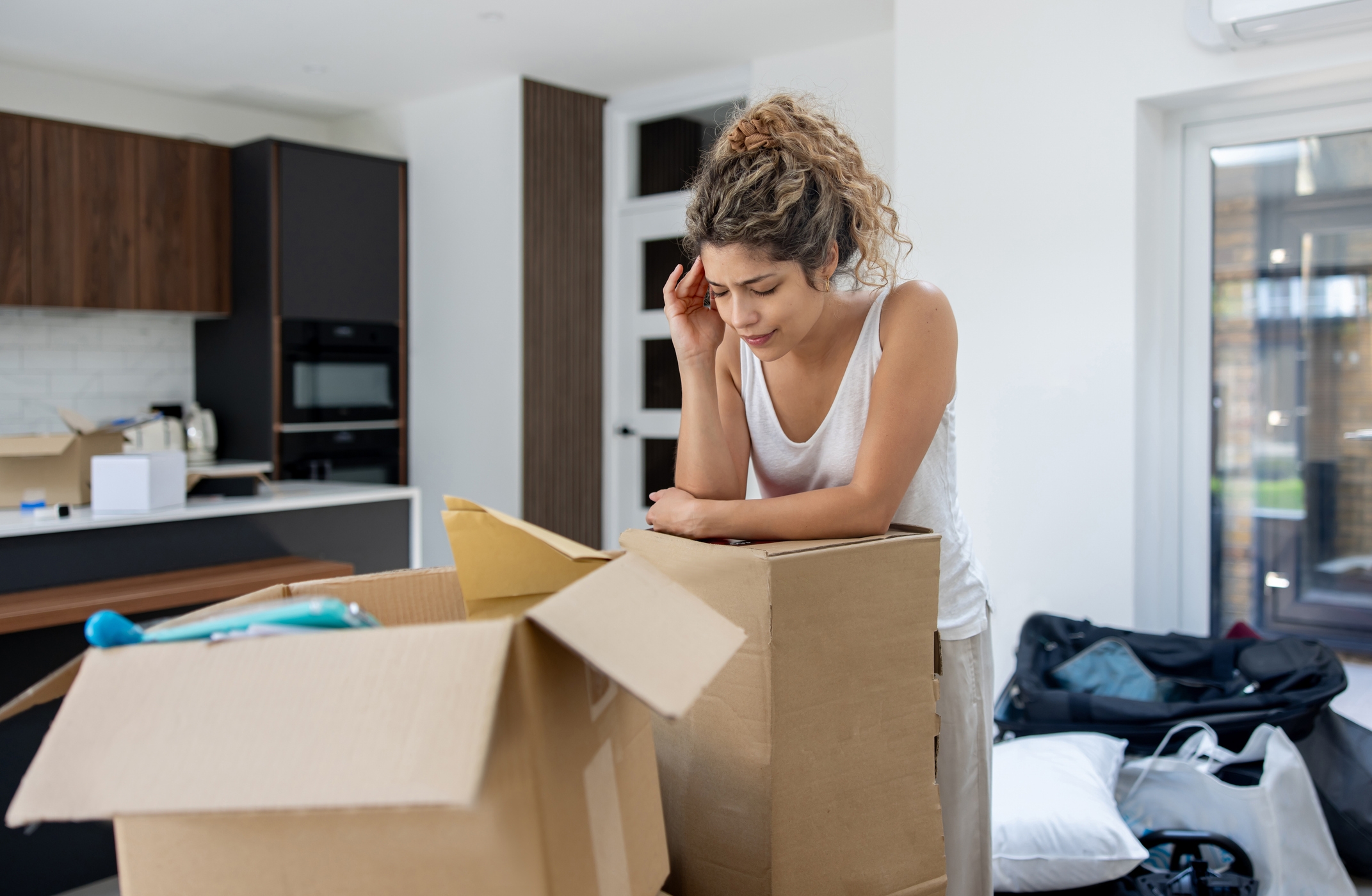Woman looking thoughtful while packing boxes in a modern kitchen, possibly preparing for a move or organizing her space