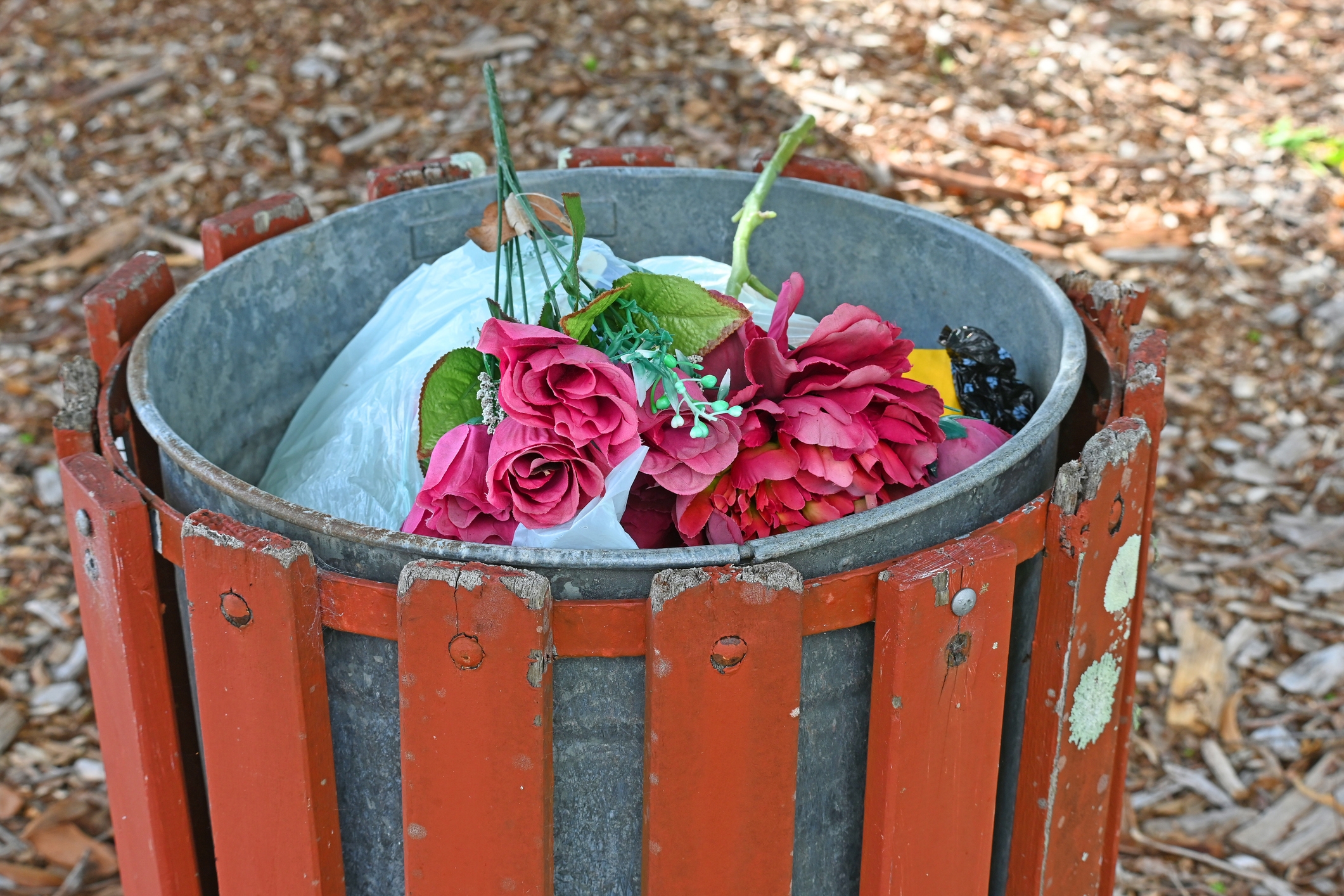Discarded bouquet of artificial roses and trash in an outdoor bin, suggesting themes of past romance or forgotten love
