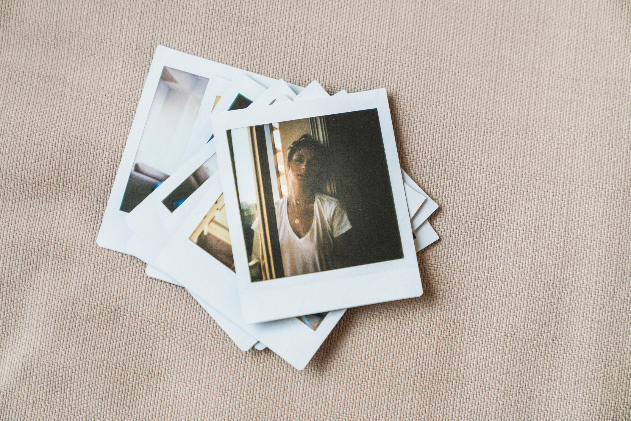 Polaroid photos scattered on a surface, featuring a person in a casual V-neck shirt, looking outside a window