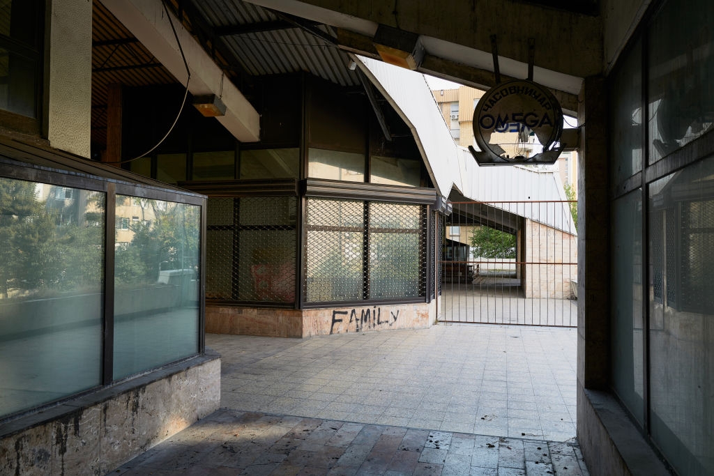 Empty hall with closed shops, graffiti reading "FAMILY," and a vintage Omega sign overhead