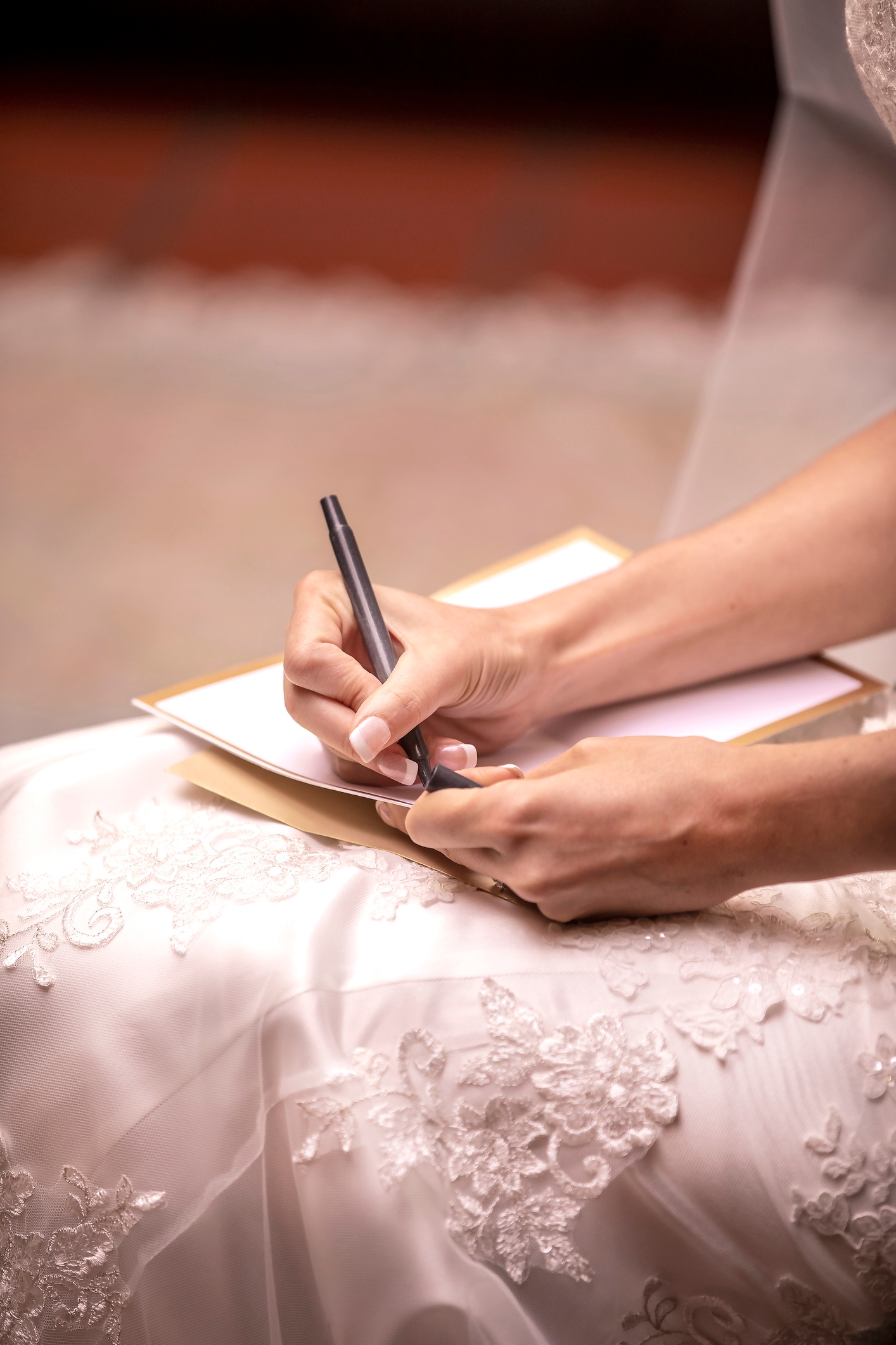 Bride in a lace gown signing a document, possibly a marriage certificate, highlighting a formal and romantic commitment moment