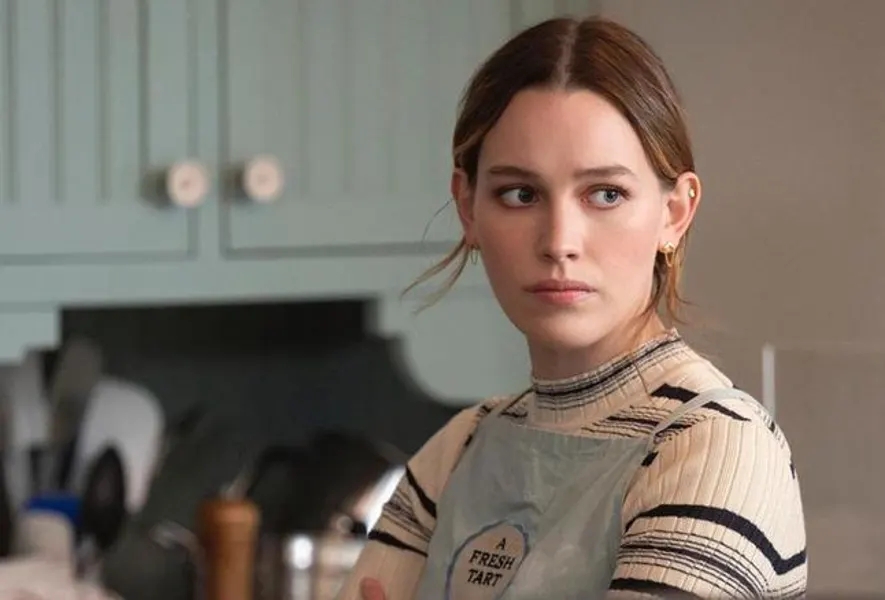 Persona en cocina con suéter de rayas y delantal; expresión seria mirando a un lado