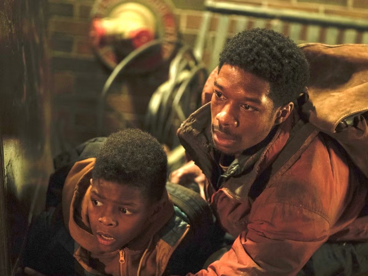 Dos personas jóvenes, vestidas con ropa casual y mochilas, se agachan en un entorno urbano, observando con atención algo fuera de cuadro