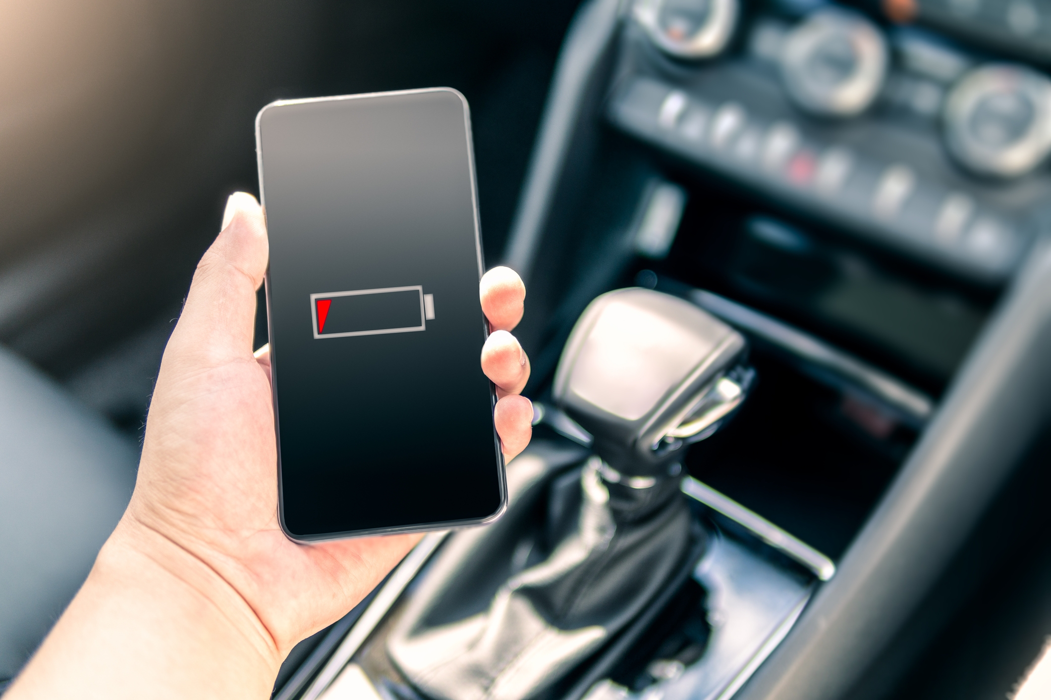 Person holding a smartphone displaying a low battery icon inside a car near the gear shift
