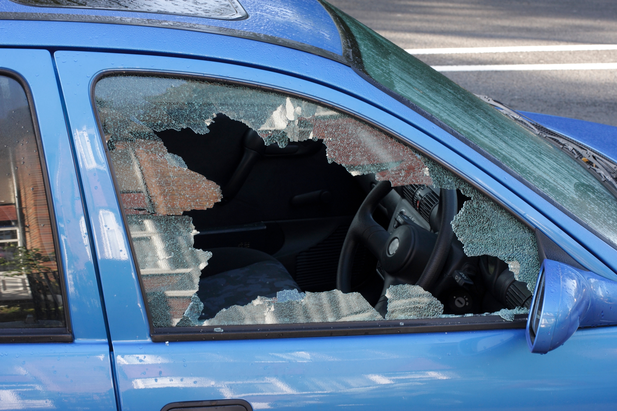 Car with shattered side window on a city street, debris visible inside