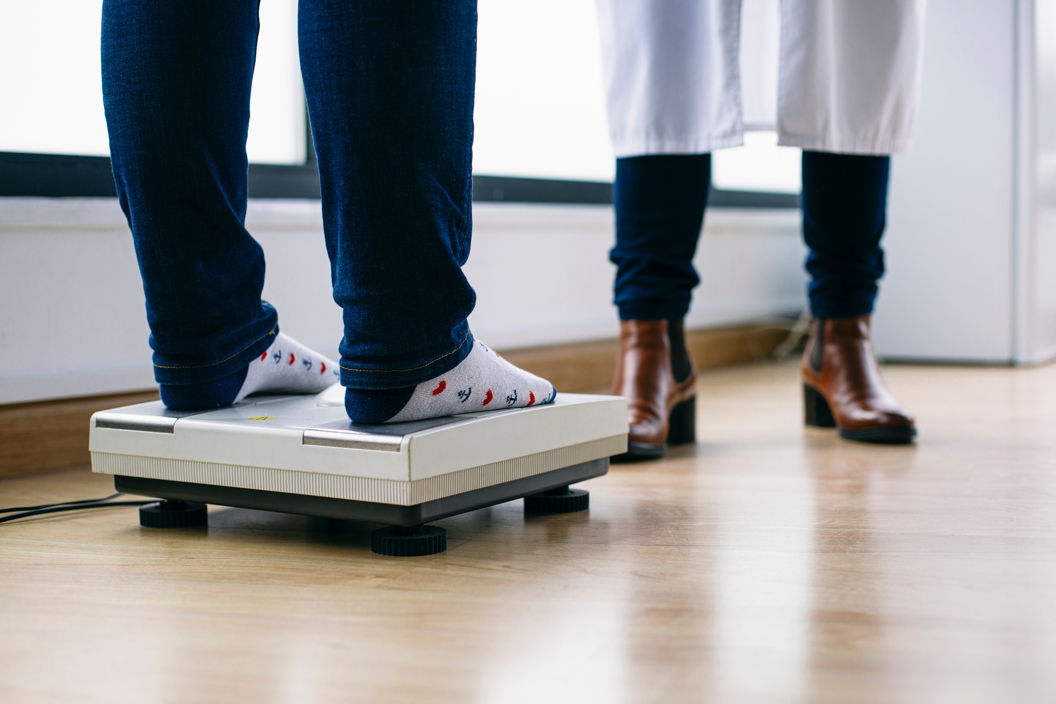Person wearing socks stands on a scale, facing a person in professional attire
