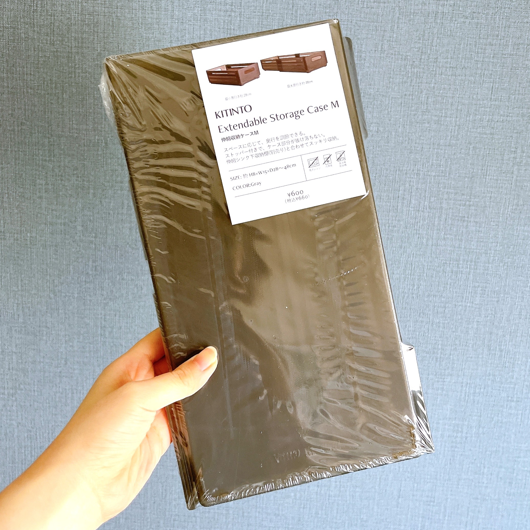 包装された伸縮式収納ケースを持つ手。ケースのラベルには商品名とサイズ情報が記載されている。