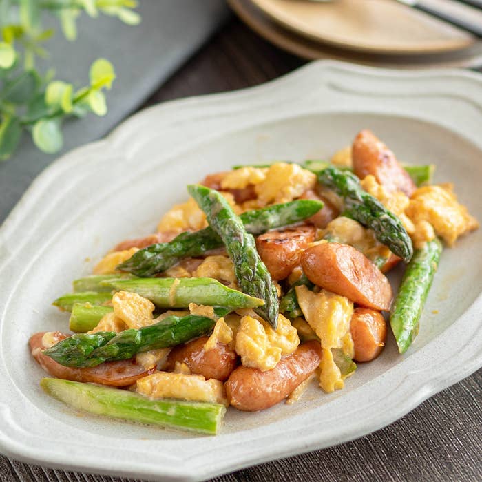 アスパラガスと卵がソーセージと一緒に盛り付けられた皿がテーブルに置かれています。