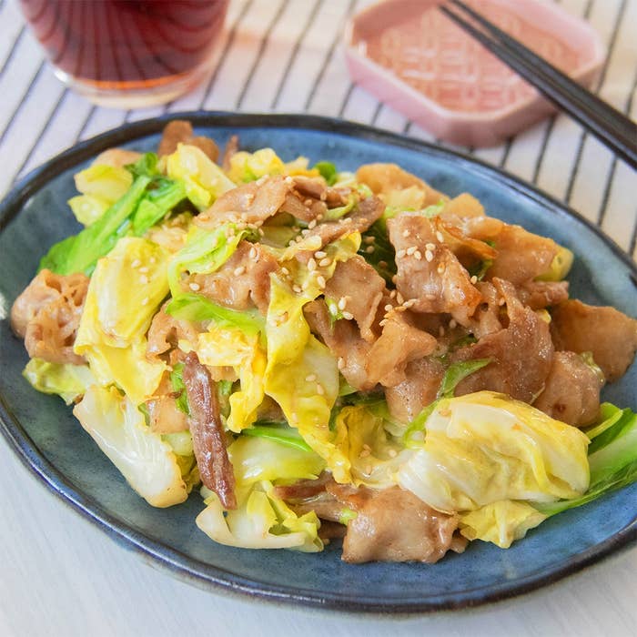 豚バラ肉とキャベツの炒め物が青い皿に盛られている。隣に箸と飲み物がある。