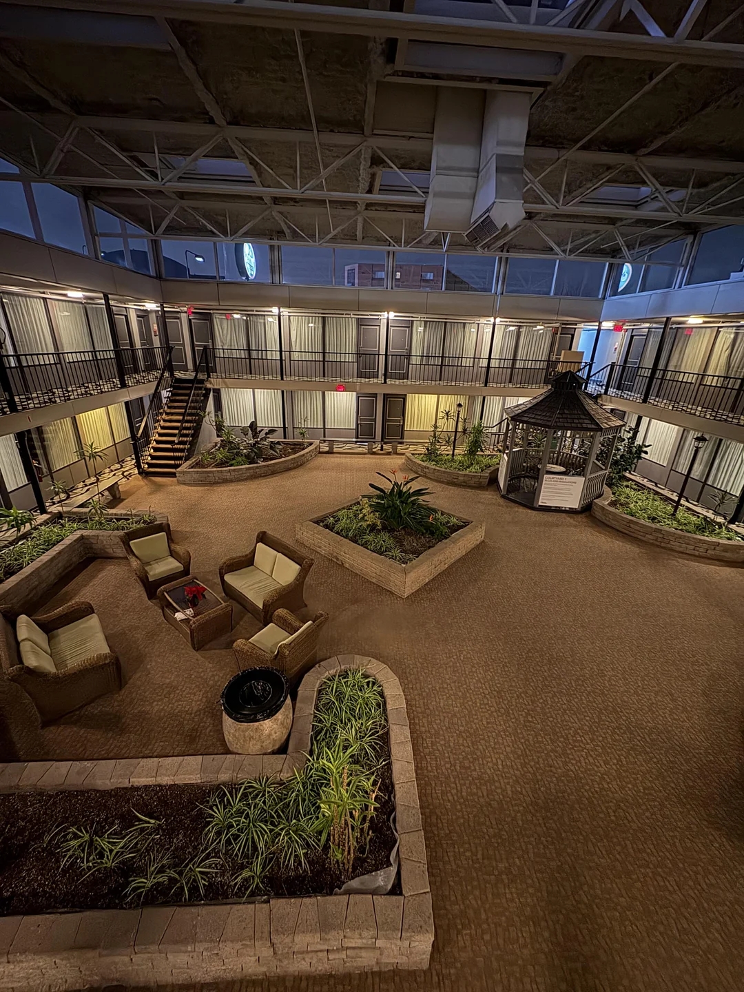 A spacious indoor courtyard with seating, plants, and a gazebo, surrounded by multi-level walkways, creating a serene, open atmosphere