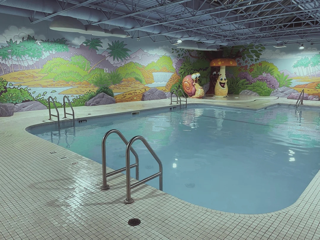 Indoor pool with mural of landscape, featuring a large snail and mushroom near one corner