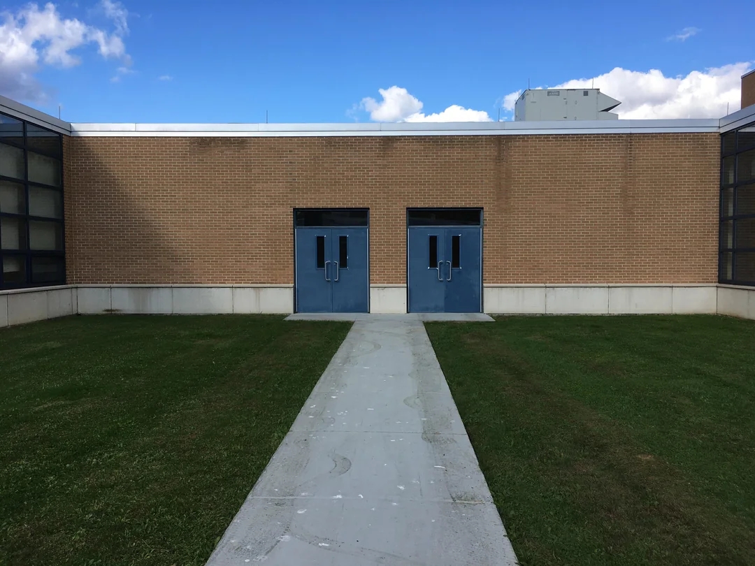Two blue double doors on a brick building with a concrete path leading through a grassy area