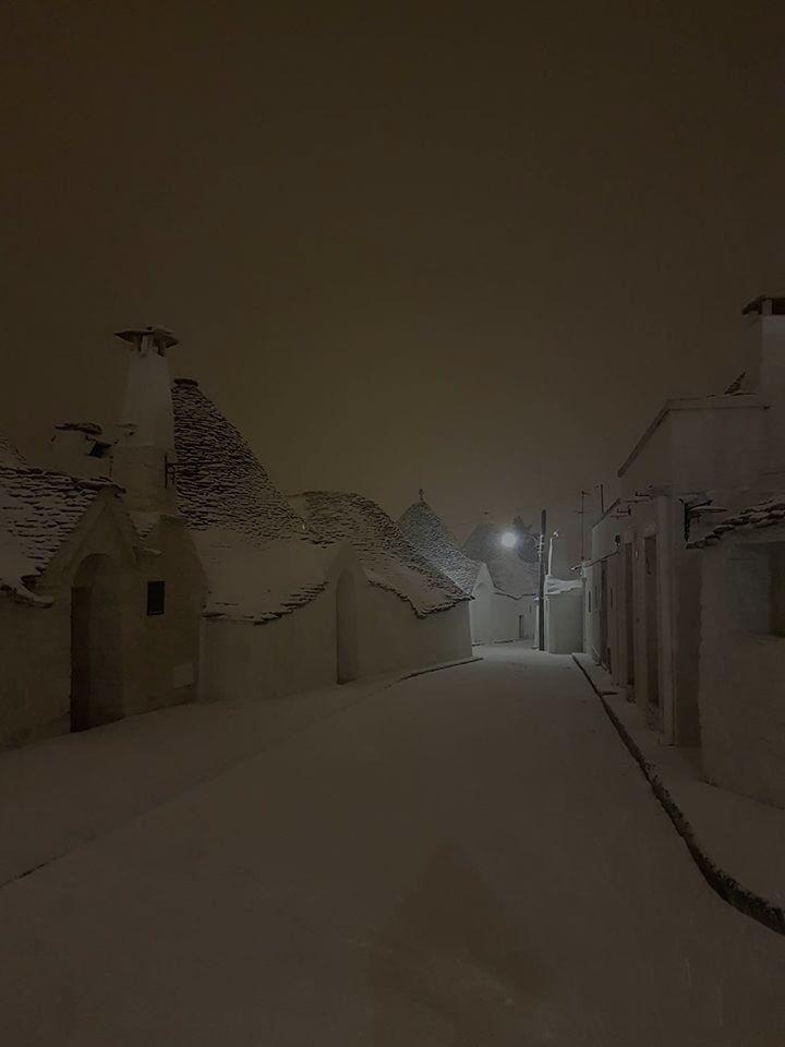 A snowy, quiet street with unique conical-roofed houses at night, softly lit by a streetlamp