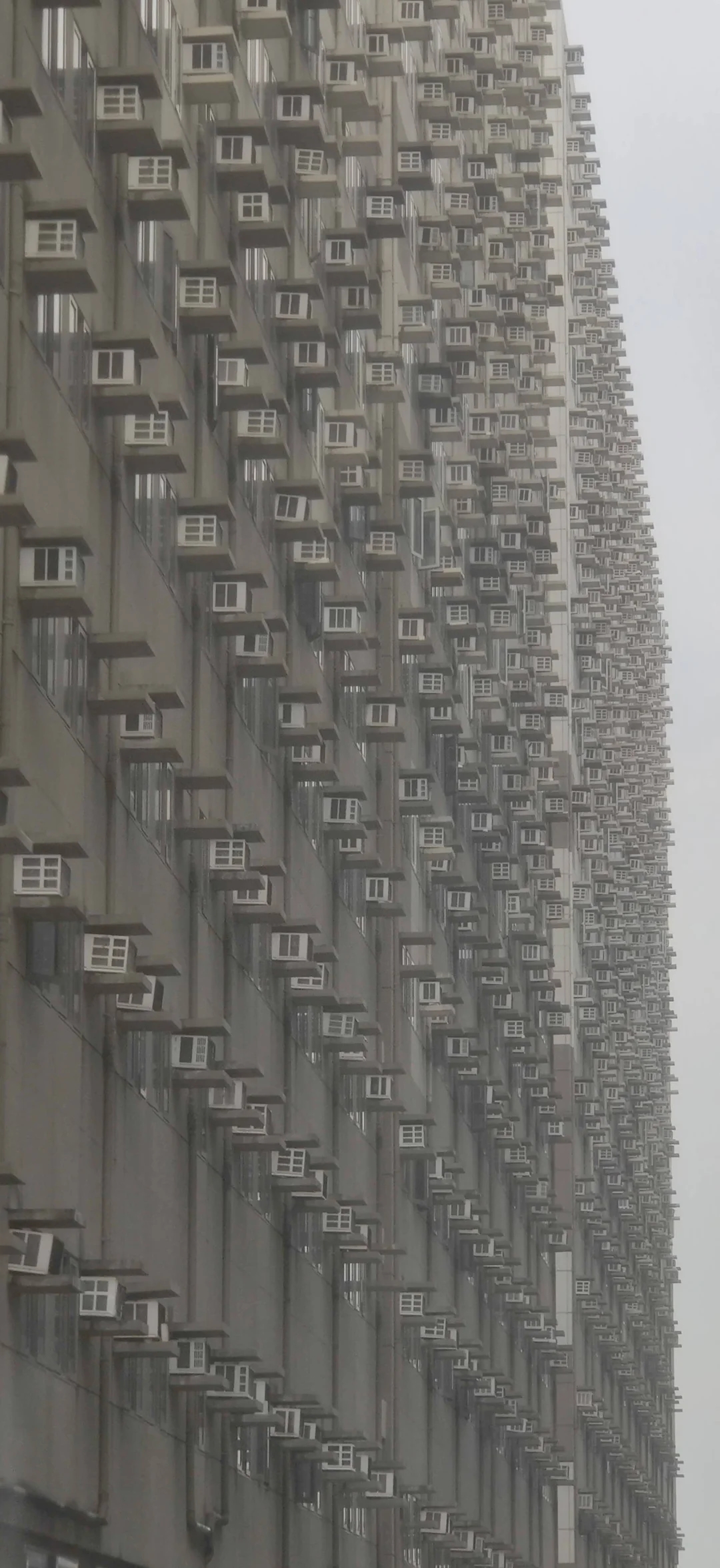 A densely populated apartment building, featuring numerous identical air conditioning units protruding from each window, creating a striking pattern