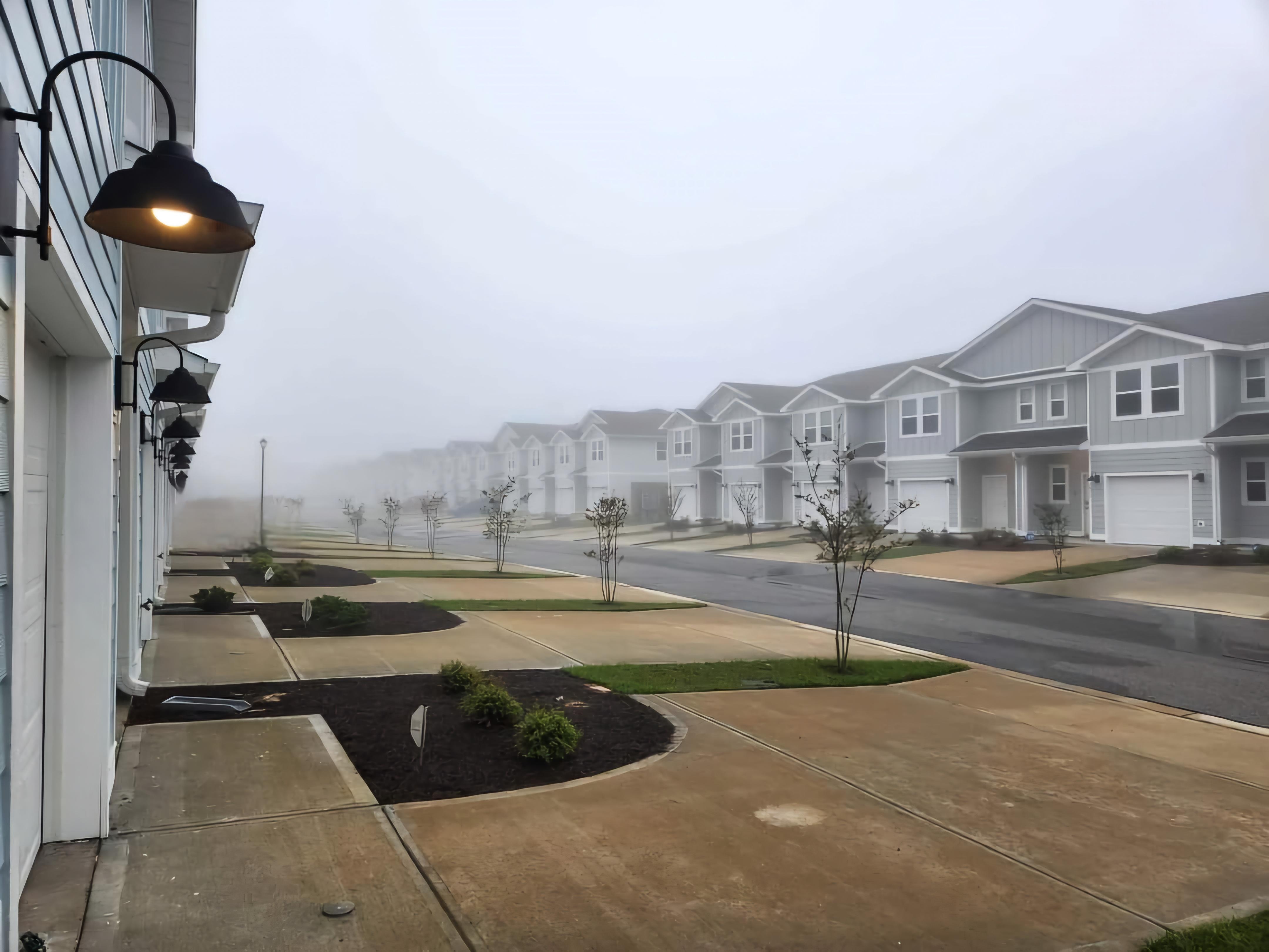 Foggy morning street scene with rows of suburban houses and empty driveways, creating a serene and quiet atmosphere