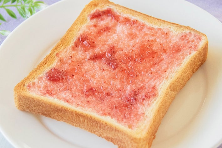 食パンにイチゴジャムが塗られたシンプルな朝食が白い皿に乗っている。