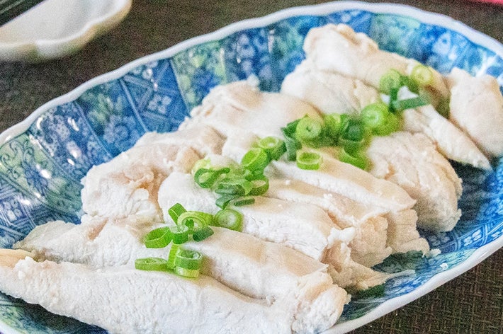 皿に盛られた鶏むね肉のサラダチキン、刻みネギが添えられている。