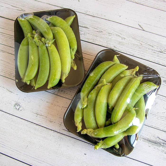 プラスチック包装に入ったさやえんどうが2パック、木製テーブルの上にある。