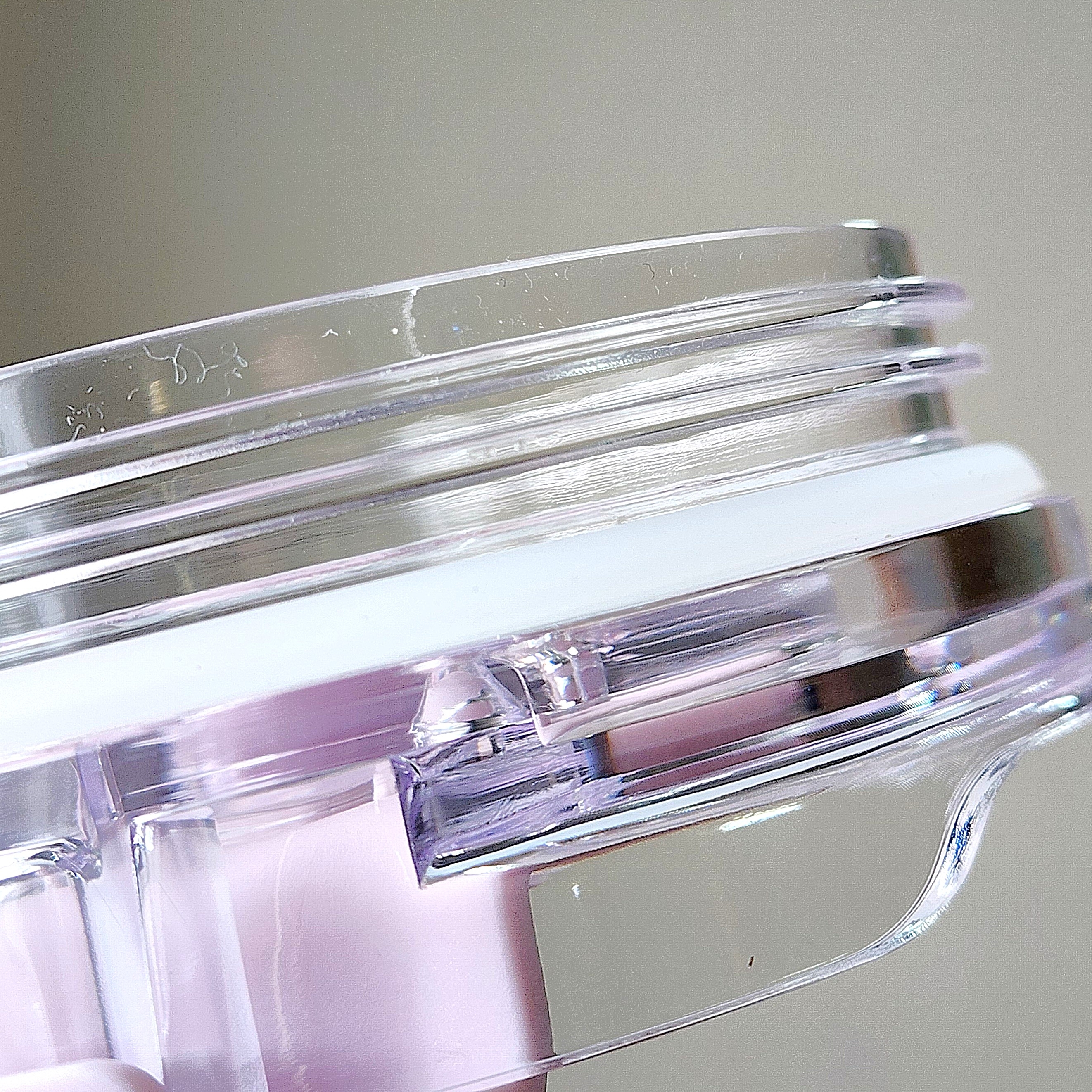 透明な円形コンテナのクローズアップ画像。コンテナはクリームまたはジェルの美容製品を入れるもののようです。