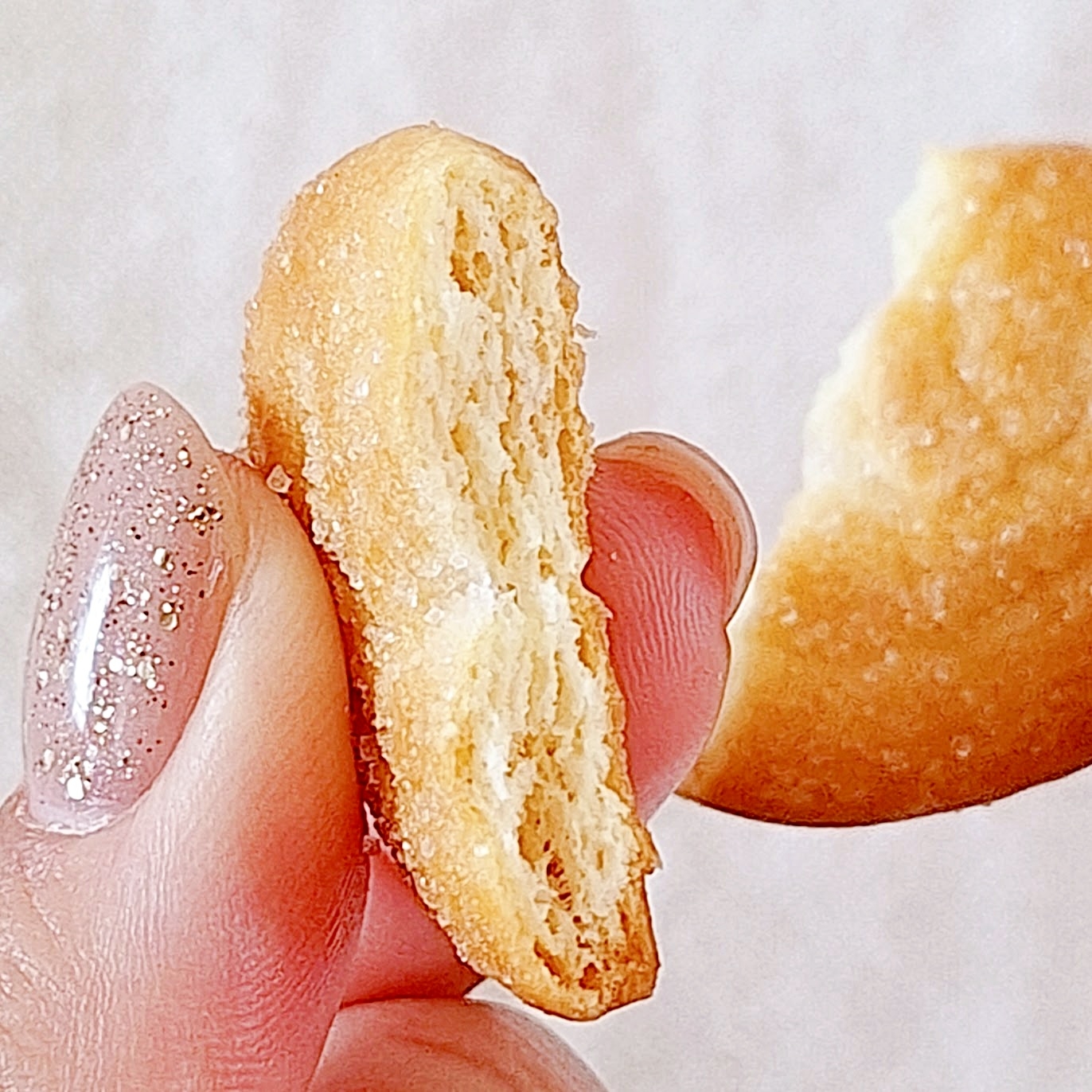 クッキーが半分に割れ、キラキラのネイルをした手で持たれています。