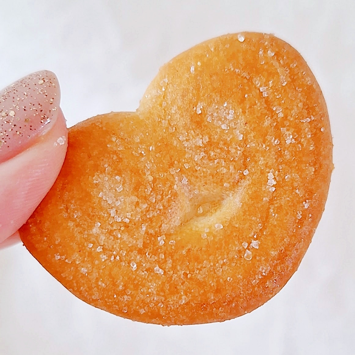 ハート形のサクサクしたクッキーを指で持っている様子。表面には砂糖がまぶされています。