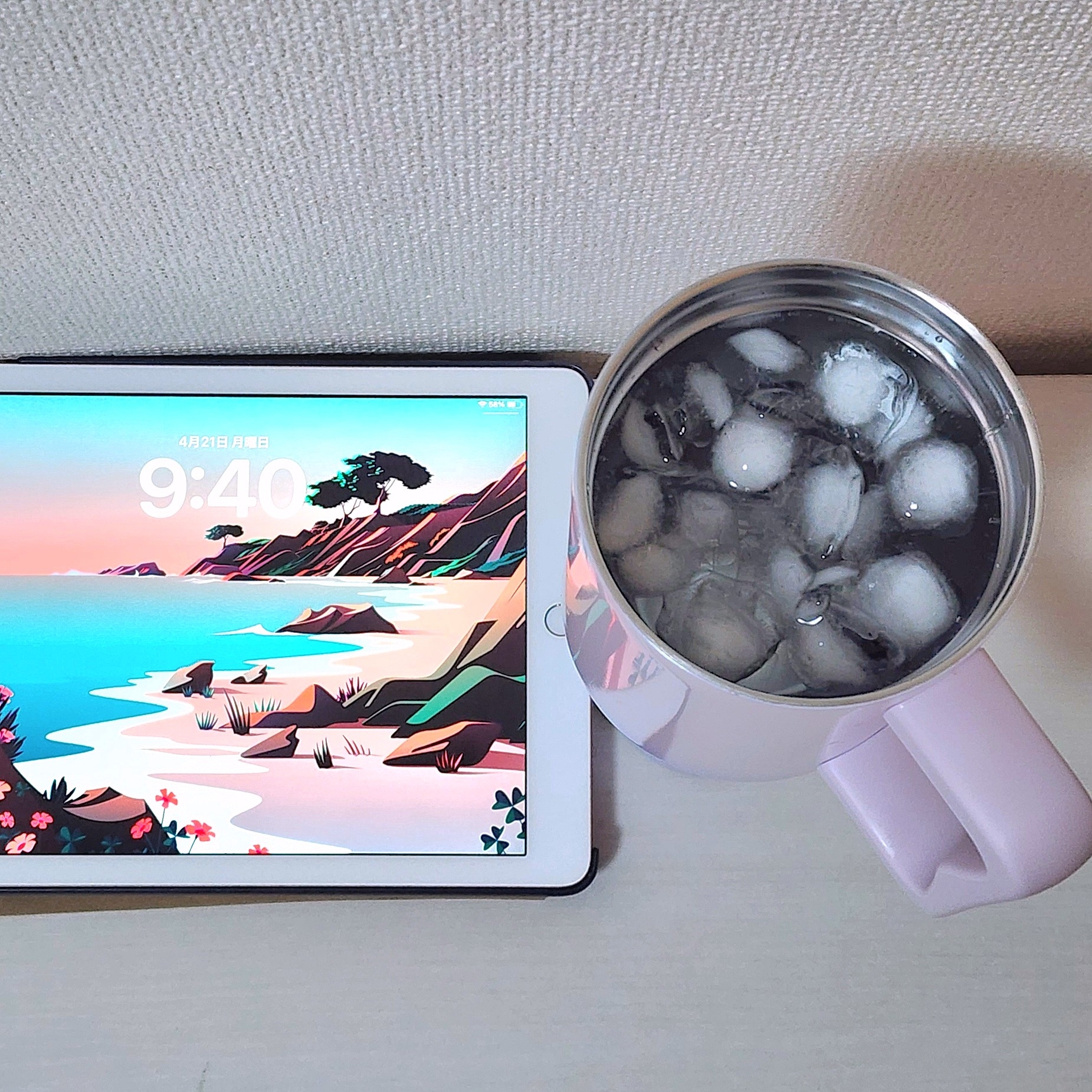 タブレットの画面に海辺の景色が表示され、隣にアイスコーヒーの入ったカップが置かれている。