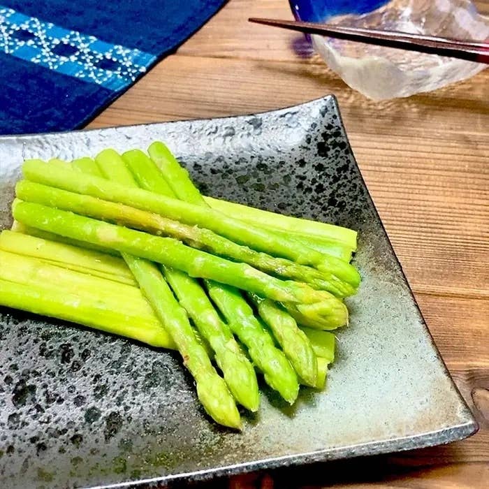 お皿に盛られた茹でたアスパラガス。隣に箸と器が配置されています。