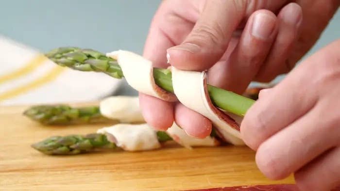 アスパラガスに薄い生地を巻いている手。