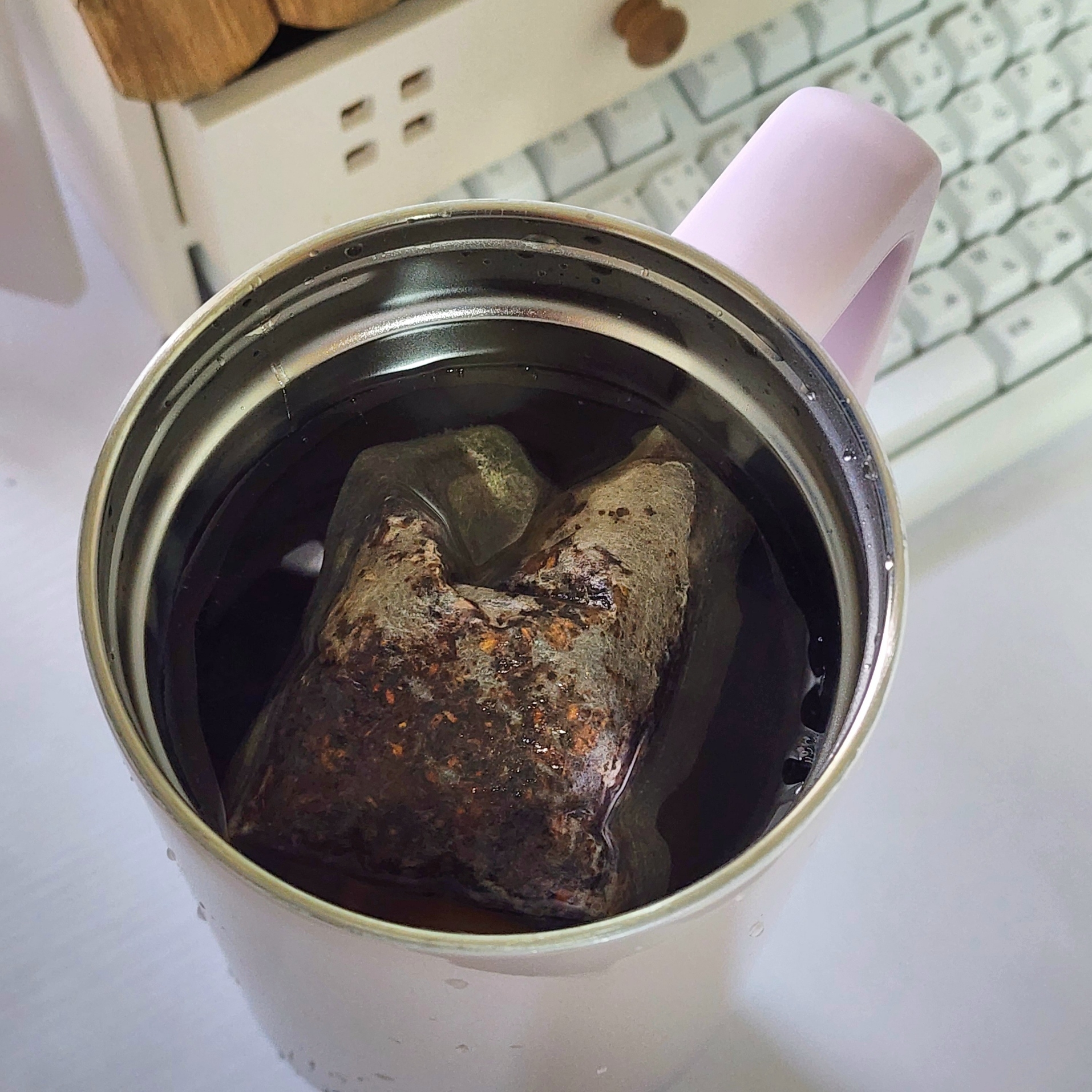 マグカップに茶葉が入ったティーバッグが熱湯で浸されている様子。背景にキーボードが見える。